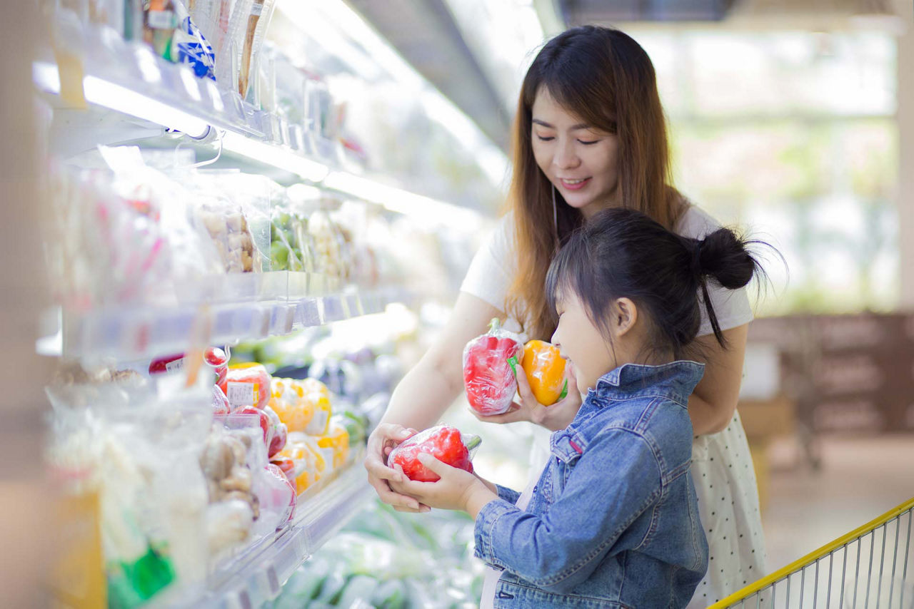 Women with daughter are choosing fresh vegetable in grocery shop.