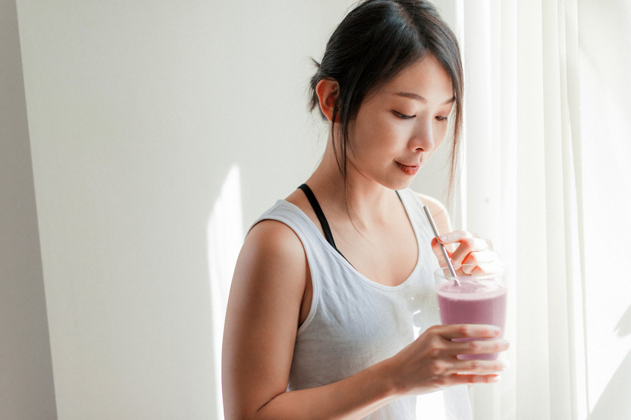 Woman drinking a meal replacement shake, Medium shot of beautiful young Asian woman drinking vegan smoothie with metal straw.
