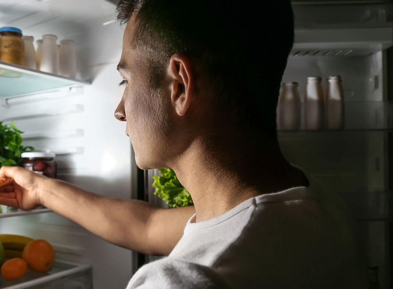 Mann schaut nachts in den Kühlschrank