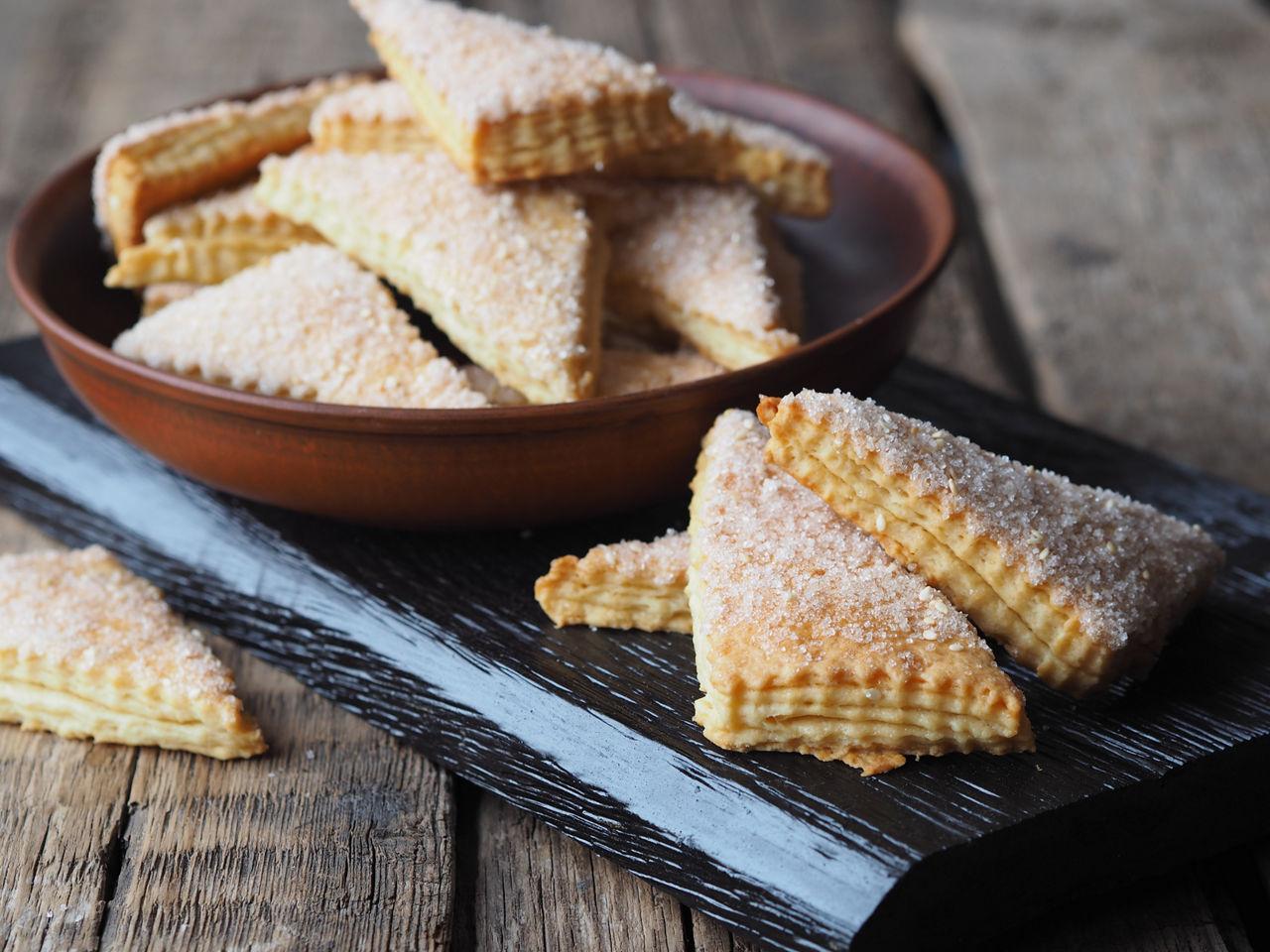 Homemade shortbread puff pastry Triangle in a brown plate on a wooden ancient background. Side view. Place for text.Topped with white sesame seeds and sugar.