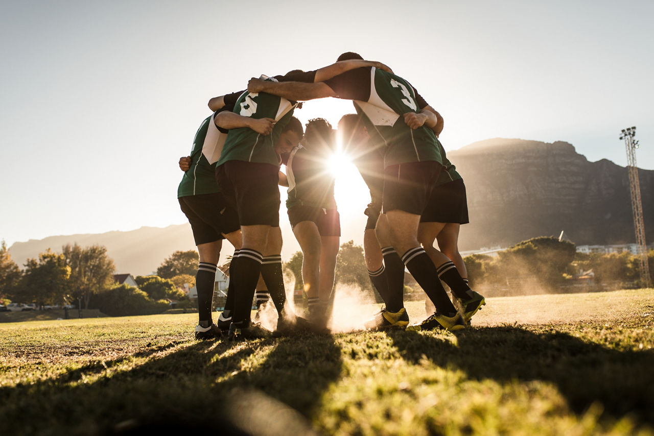 Rugby team standing in a huddle and rubbing their feet on ground.