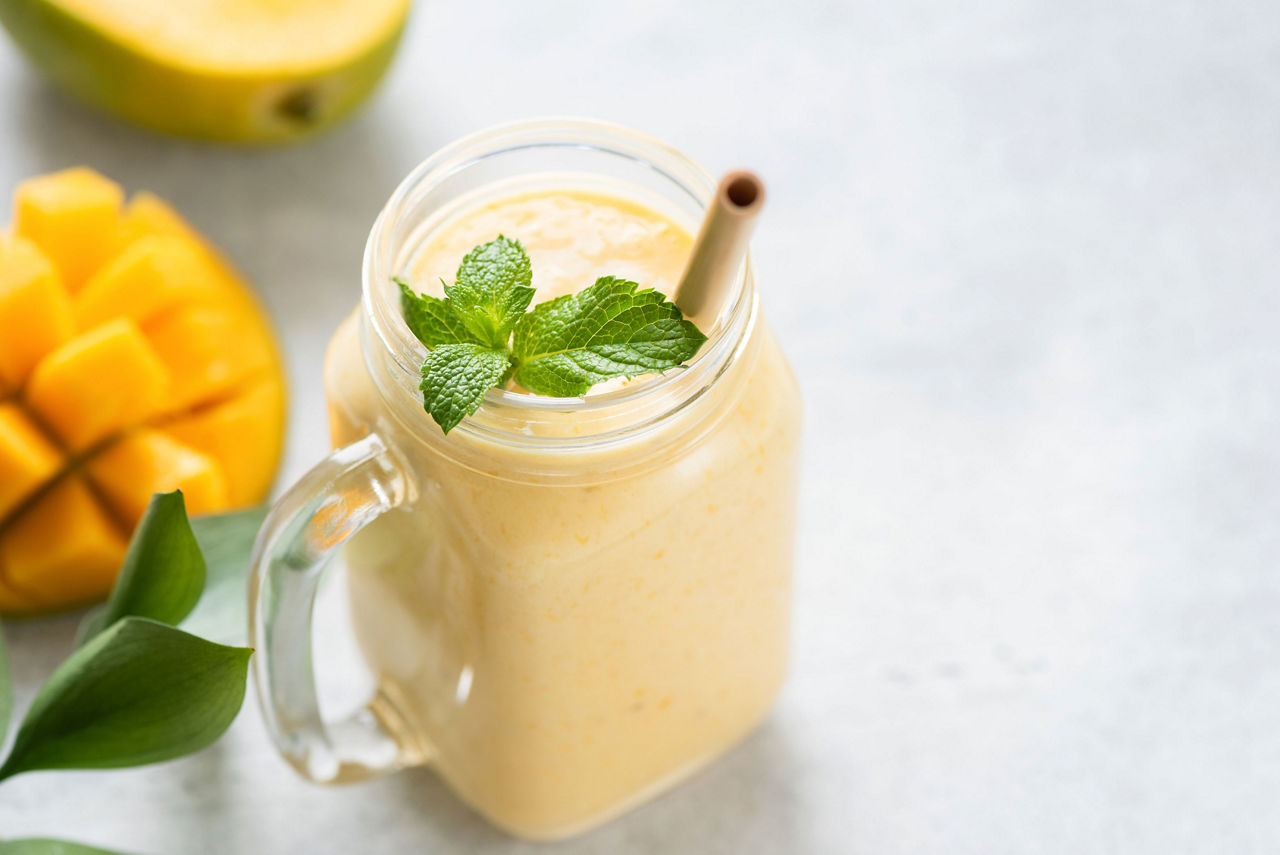 Protein shake with mango and yogurt, Mango lassi in a glass on grey concrete background table, copy space for text or design. Mango yogurt smoothie