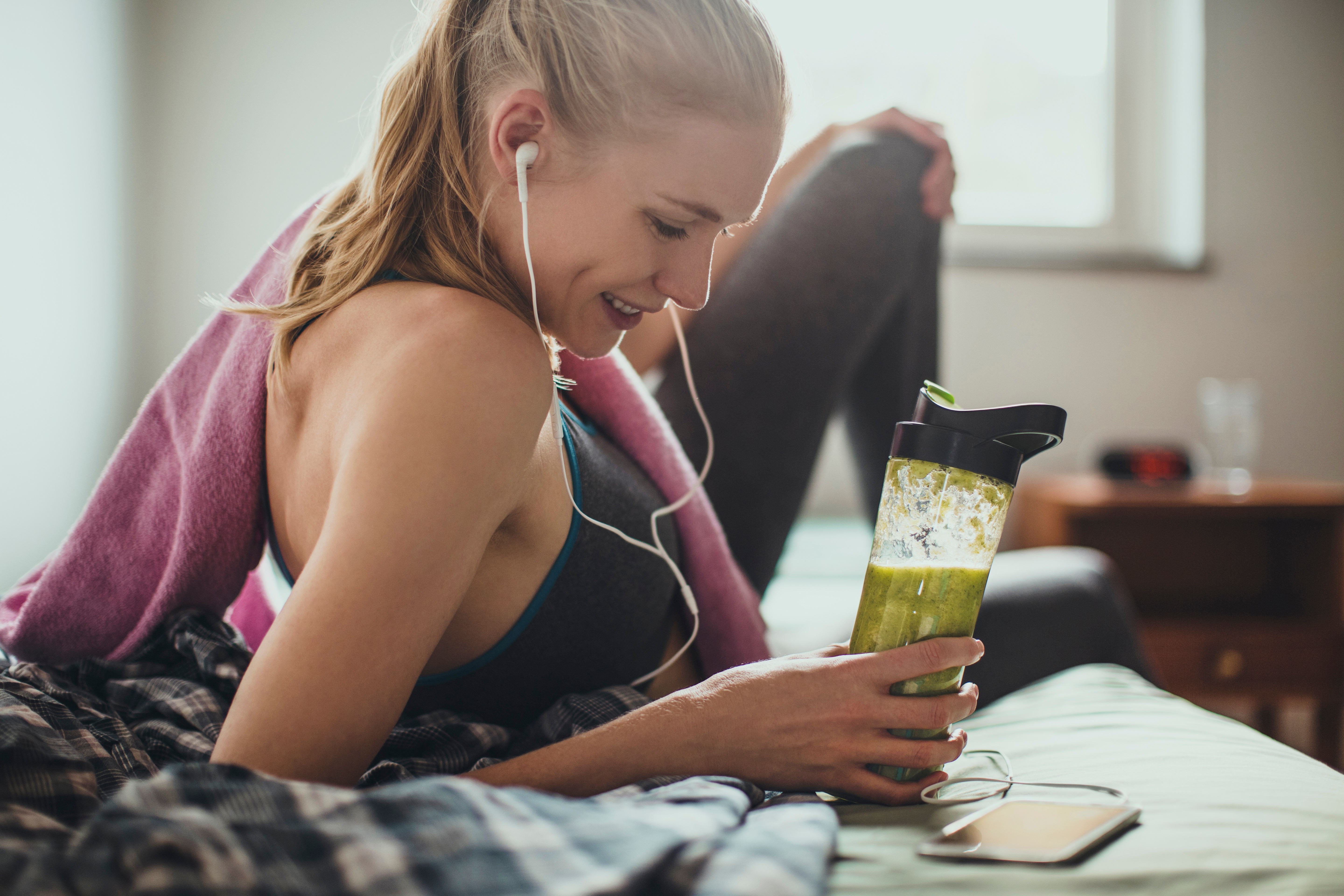 Žena poslouchá hudbu a drží láhev s zeleným smoothie
