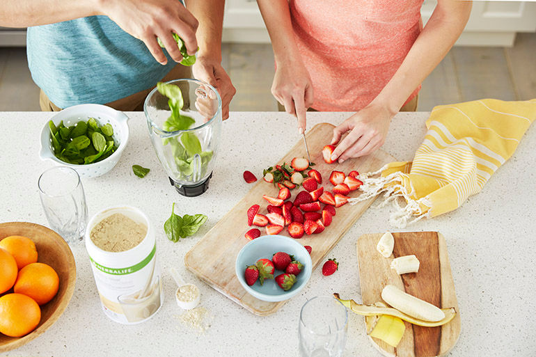 1 woman cutting Strawberry and one man putting something in Blender Glass