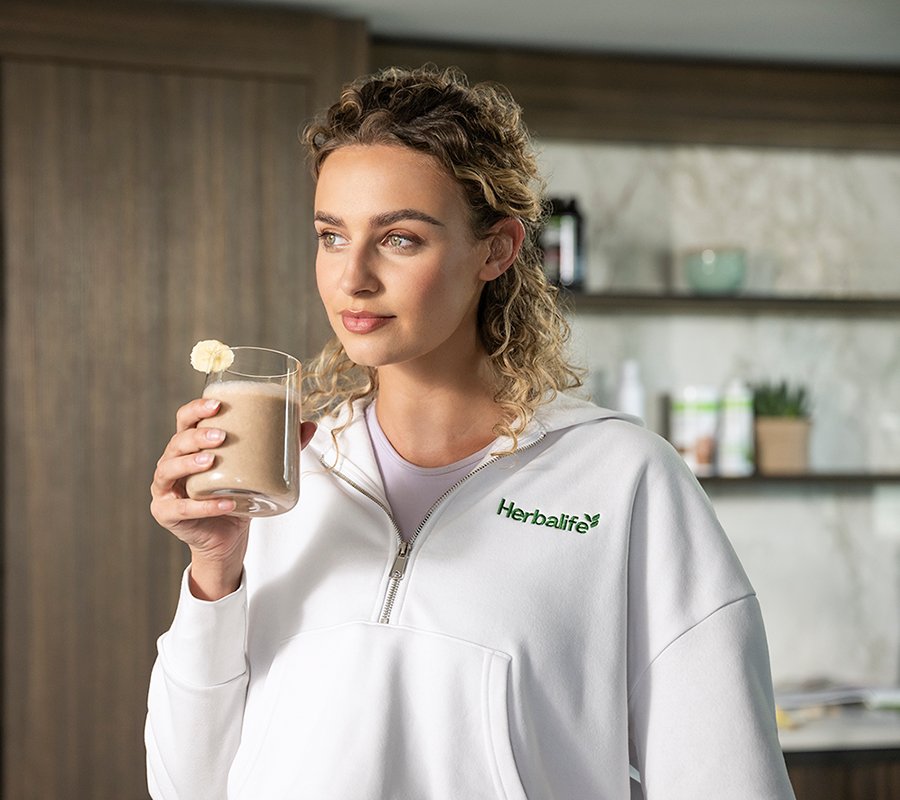Mujer sonriendo y disfrutando de un batido de proteínas Herbalife en la cocina.