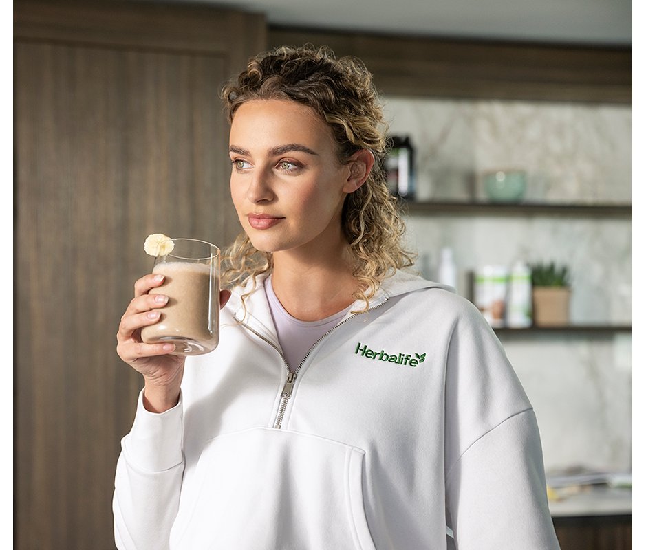 Donna che sorride e si gode un frullato proteico Herbalife in cucina.