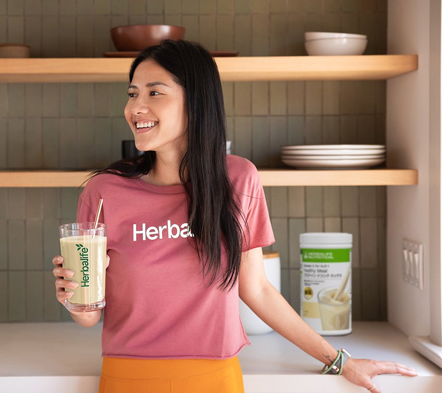 ស្ត្រី​ដែលញញឹម ហើយ​រីករាយ​នឹងអាហារក្រឡុក​ប្រូតេអ៊ីន​រសជាតិ​វ៉ានីឡារបស់ Herbalife នៅក្នុង​ផ្ទះបាយ។
