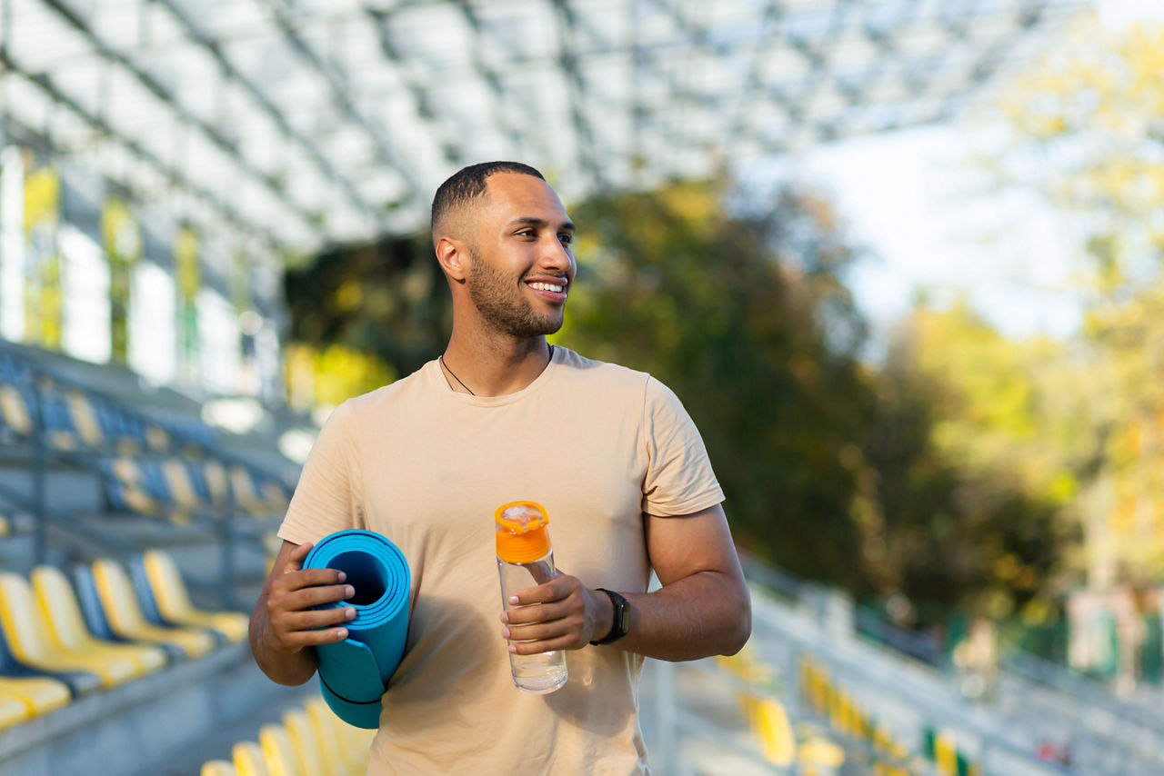 Man holding a water bottle and yoga mat