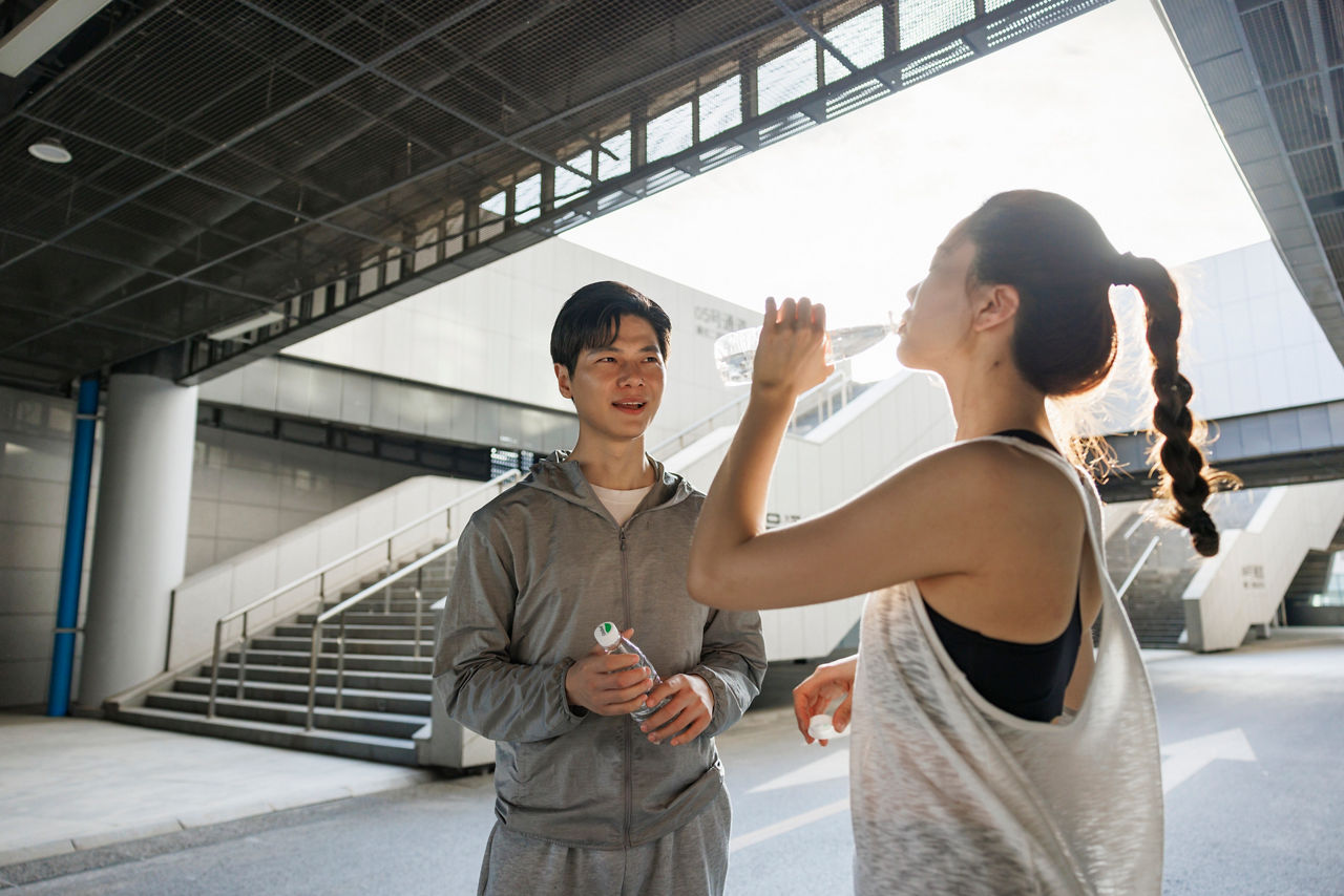 A young asian couple, wearing sportswear. In the urban scene, exercise. After the exercise, they were drinking water and chatting.The shooting place is in Zhengzhou, China, which is the citizen fitness center. It is a public open area.
