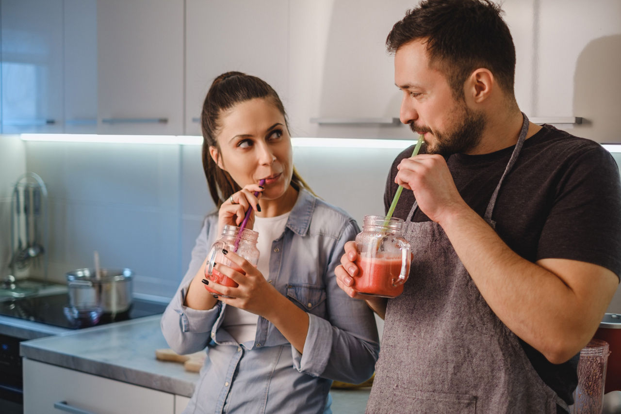 Couple flirting in the kitchen while drinking smoothie with a straw