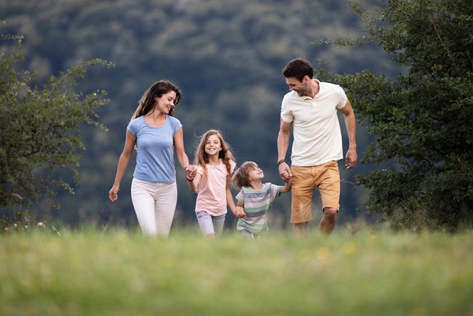 Happy parents and their small kids holding hands while walking and talking in nature. Copy space.