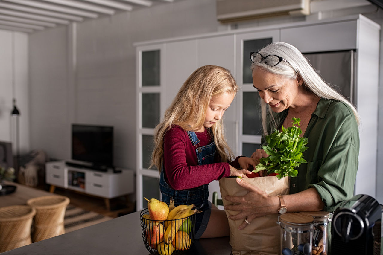 Grandmother and her granddaughter holding grocery shopping bag with vegetables at home 