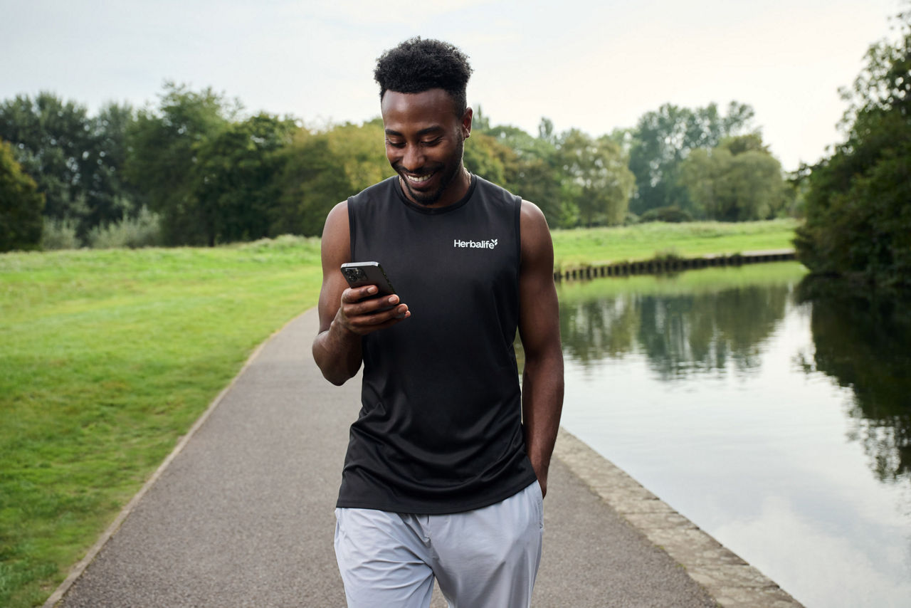 Man smiling at phone whilst walking in the park