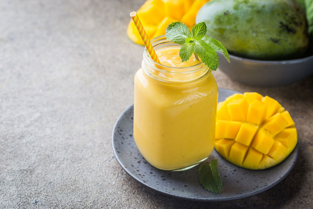 Refreshing and healthy mango smoothie in a glass with fresh fruit over stone background