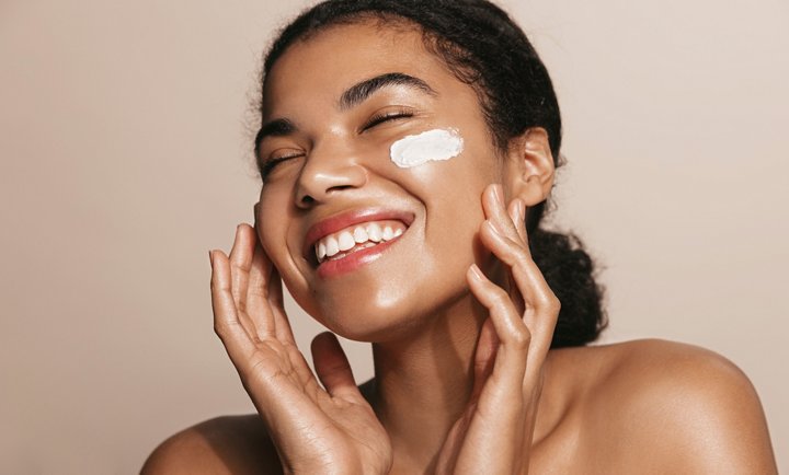 Smiling woman using skincare product. Female applying facial cream.
