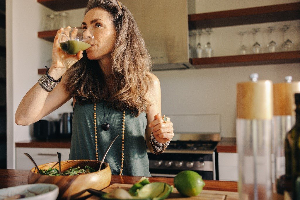 Donna che beve in cucina un succo verde salutare