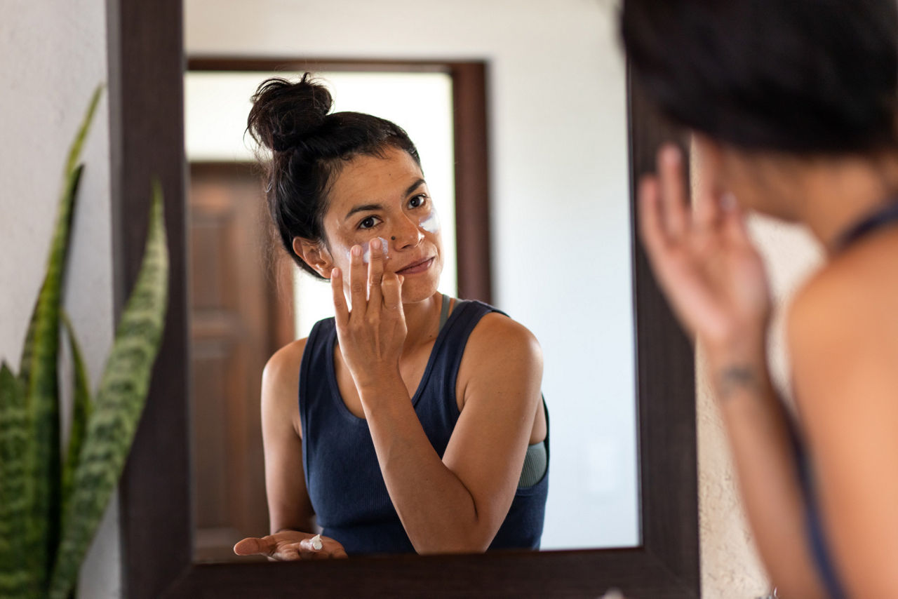 Woman applying white sunblock to her face while looking in the mirror