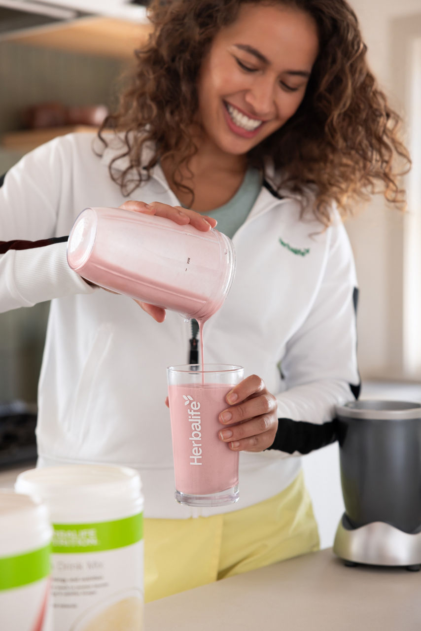Woman pouring a wildberry shake with Formula 1 Shake product canisters on the counter.
