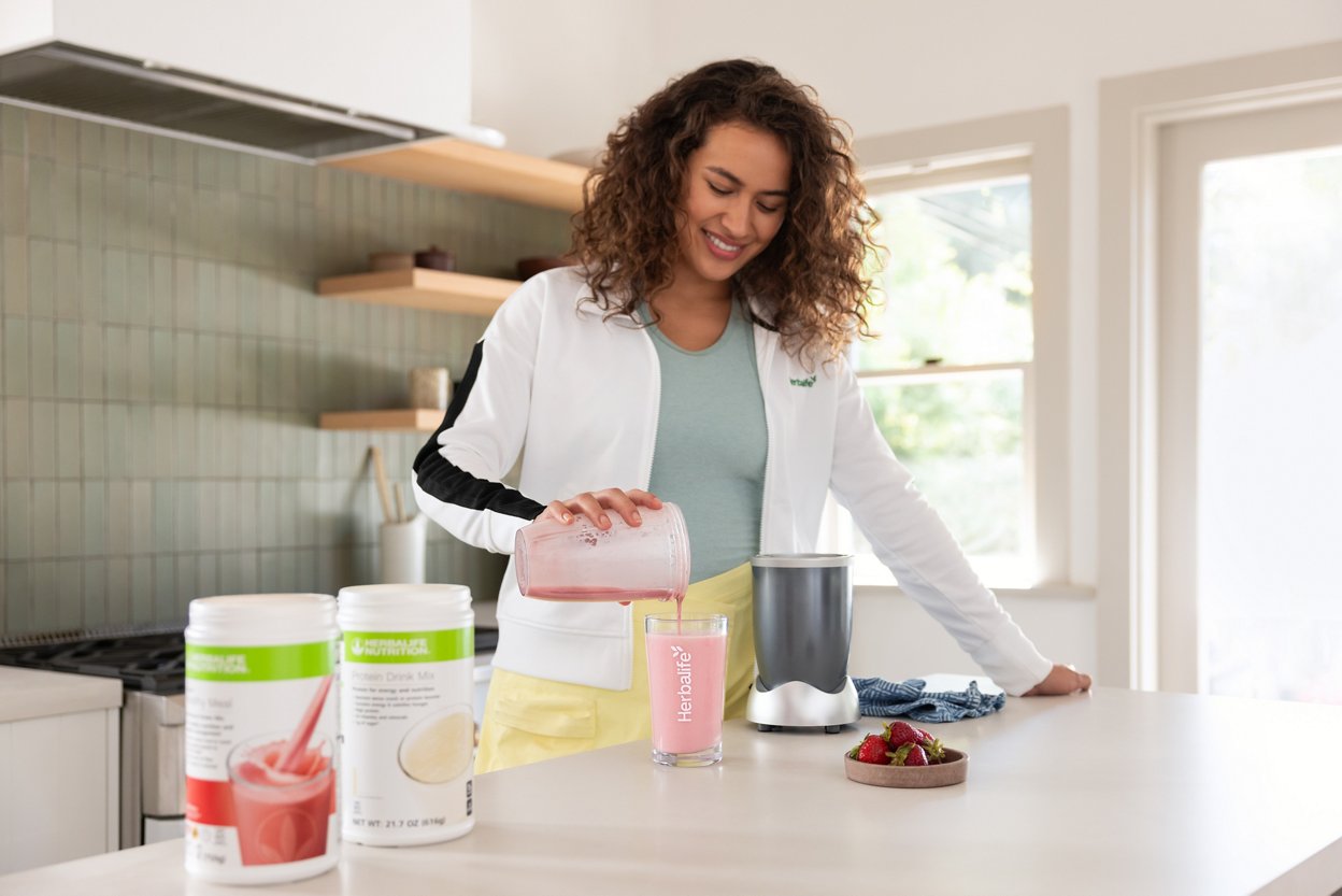 Woman pouring a Formula 1 Wildberry Flavor Shake in her kitchen with F1 product canisters on the counter.