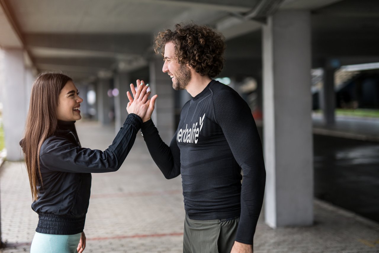 Happy young athletic couple running outdoors under the bridge and giving high fives to each other