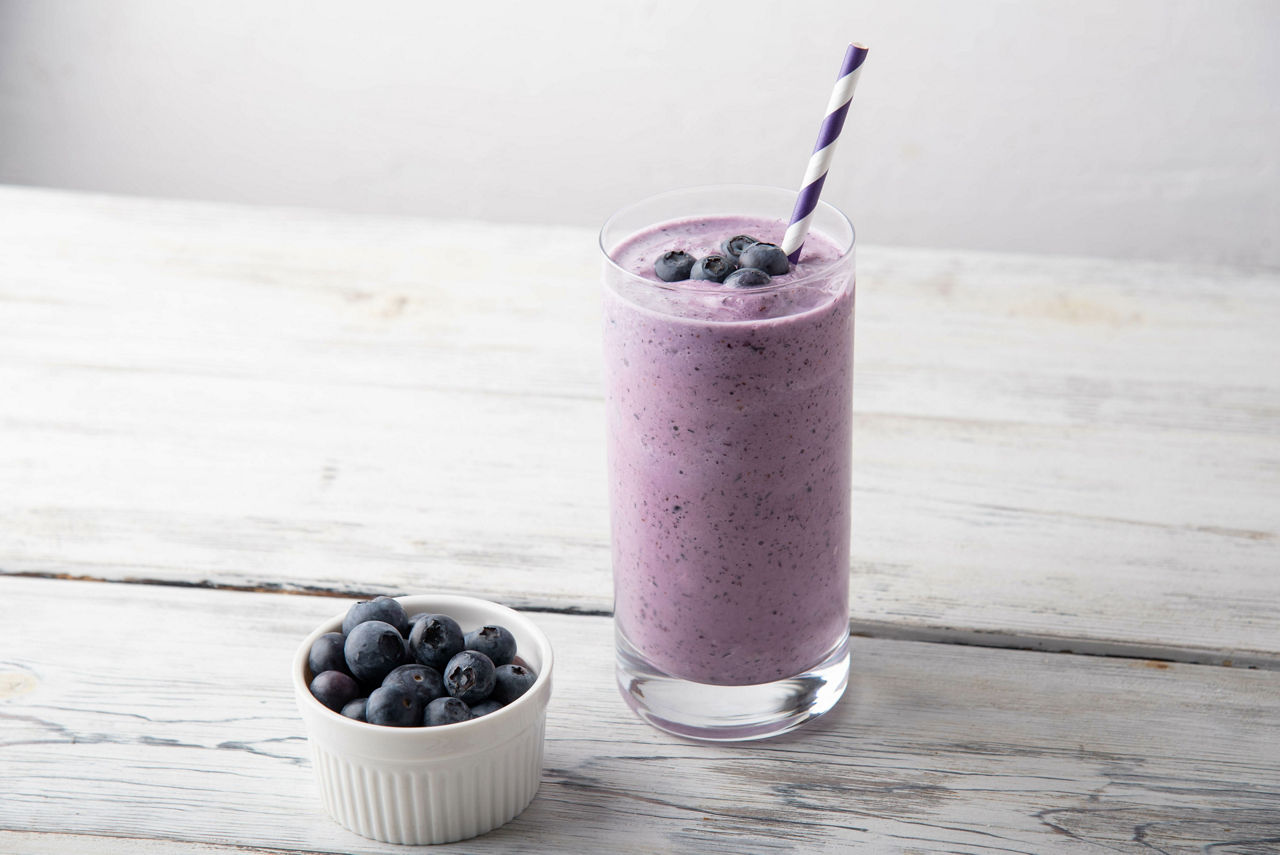A glass of blueberry Formula 1 protein shake, blueberry smoothie on white background