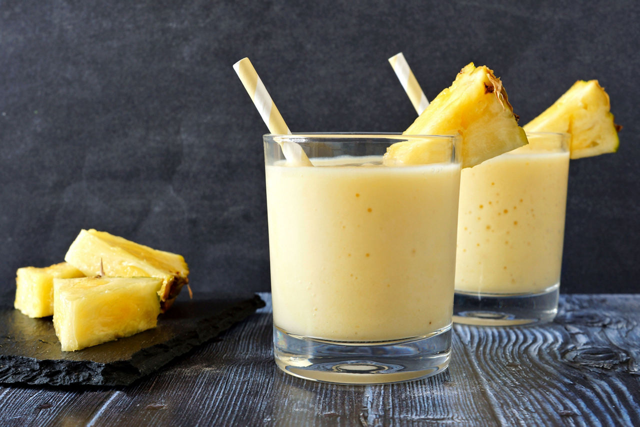 Protein shake with pineapples and yogurt, Two glasses of tropical pineapple smoothie against a dark background