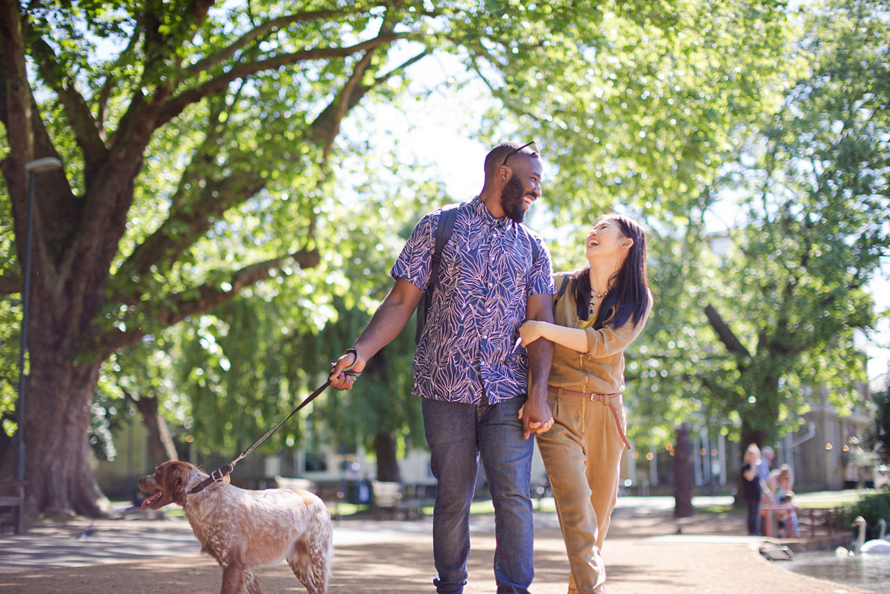 Happy young couple walking dog in sunny park