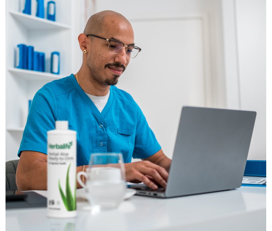 A man in the office working on his laptop, an Herbalife Herbal Aloe Ready-to-Drink Aloe bottle on his desk