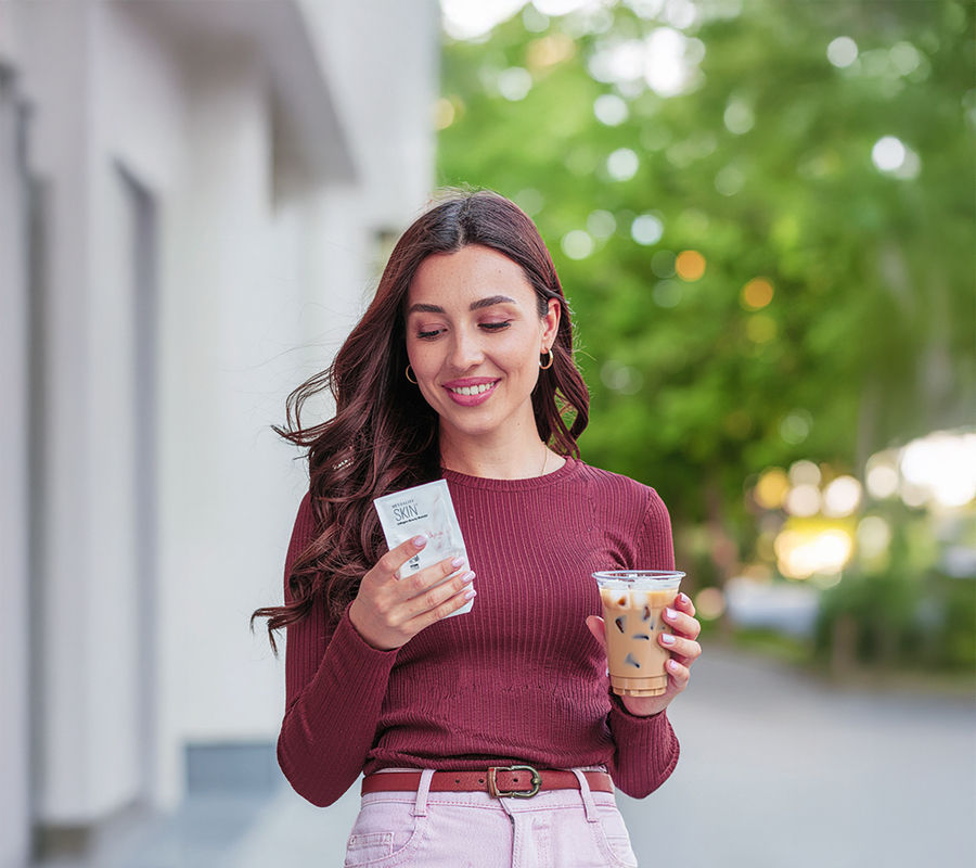 Woman drinking coffee mixed with collagen powder outdoors and holding a collagen powder sachet