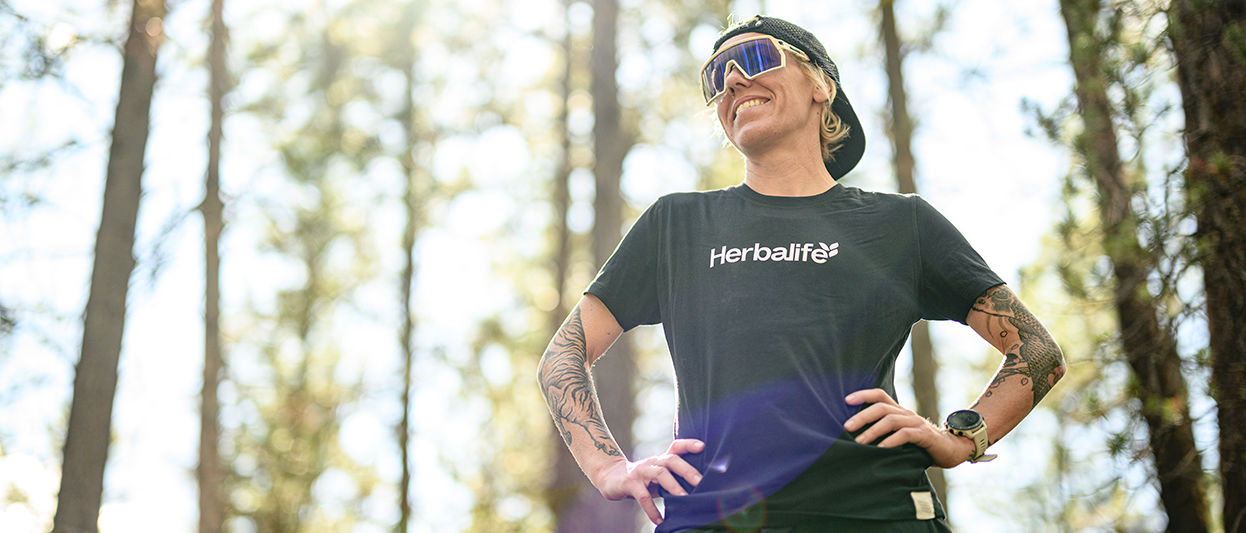 ​​​​Heather Jackson, elite endurance athlete and Herbalife-sponsored runner, stands outdoors in running gear and hydration vest, looking focused before a trail run. 