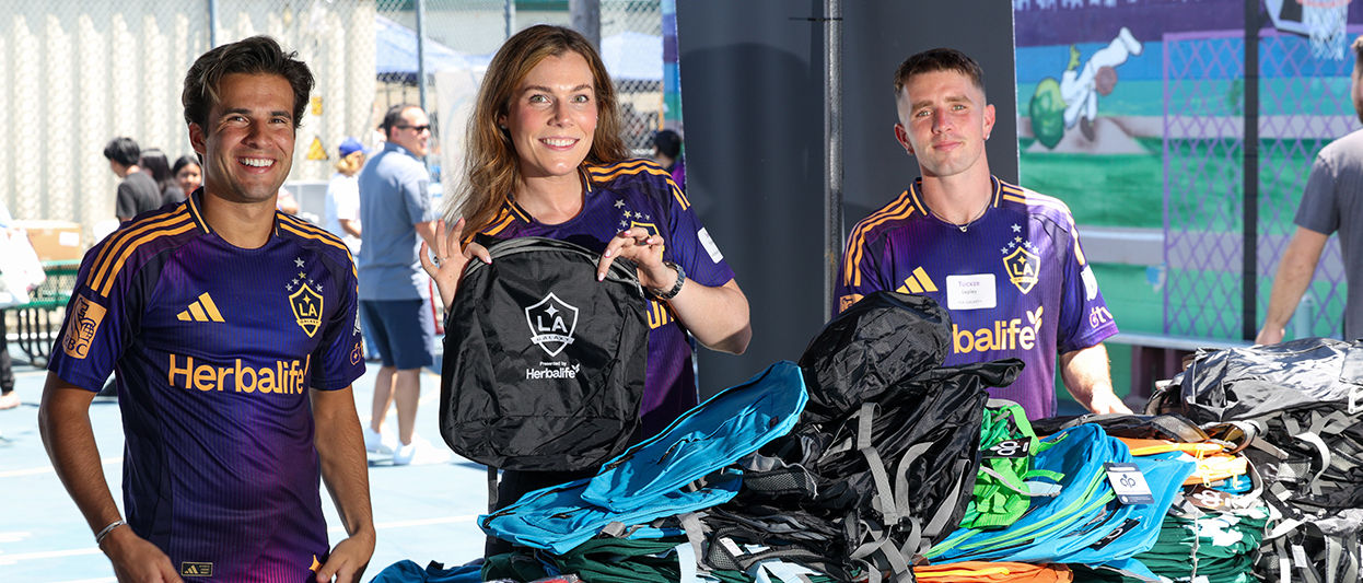 LA Galaxy midfielder Riqui Puig, Herbalife vice president of regional sales and business development Samantha Holway, and forward Tucker Lepley help distribute backpacks to kids and families at the annual Back-to-School event in South Los Angeles.
