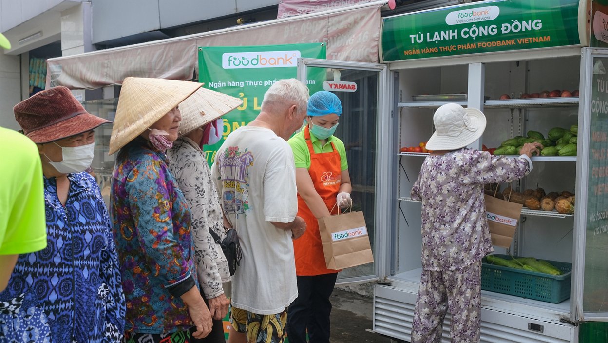 Orang-orang mengantre sambil membawa tas di dekat spanduk 'Global FoodBanking Network', yang memamerkan bantuan pangan.
