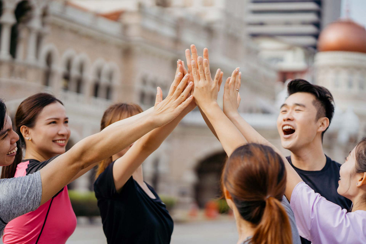 Group of young asian man and woman in sports clothing giving each other high five and smiling while exercising outdoors
