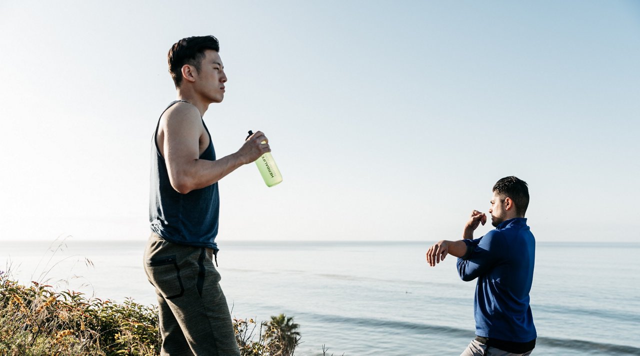 2 Males in workout clothes, one stretching shoulder, another holding an Herbalife Nutrition water bottle.