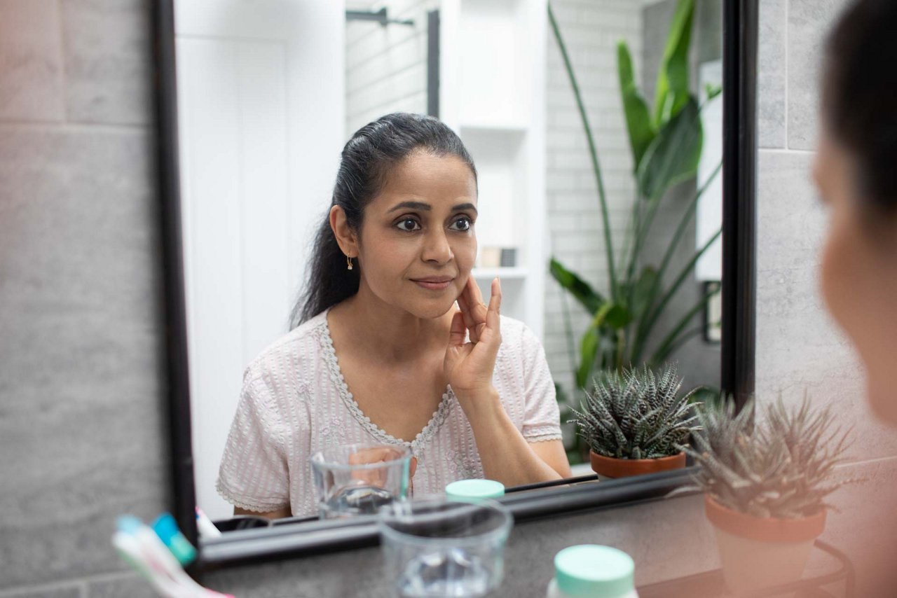 UK, London, Woman touching face reflected in bathroom mirror