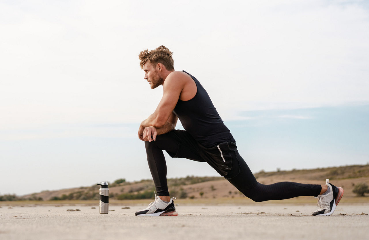 Photo of athletic young sportsman doing exercise while working out on summer beach