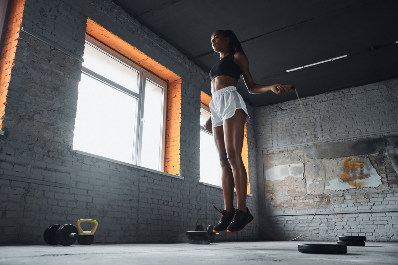 Full length of confident young woman jumping with rope in gym