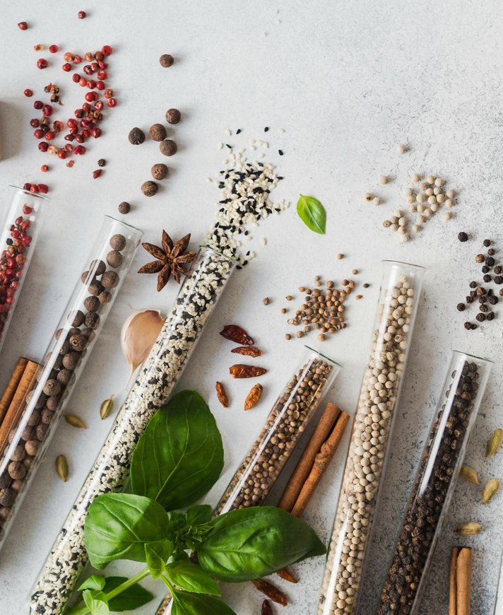Various spices in glass test tubes and fresh herbs on gray background. Set of various spices and herbs flat lay