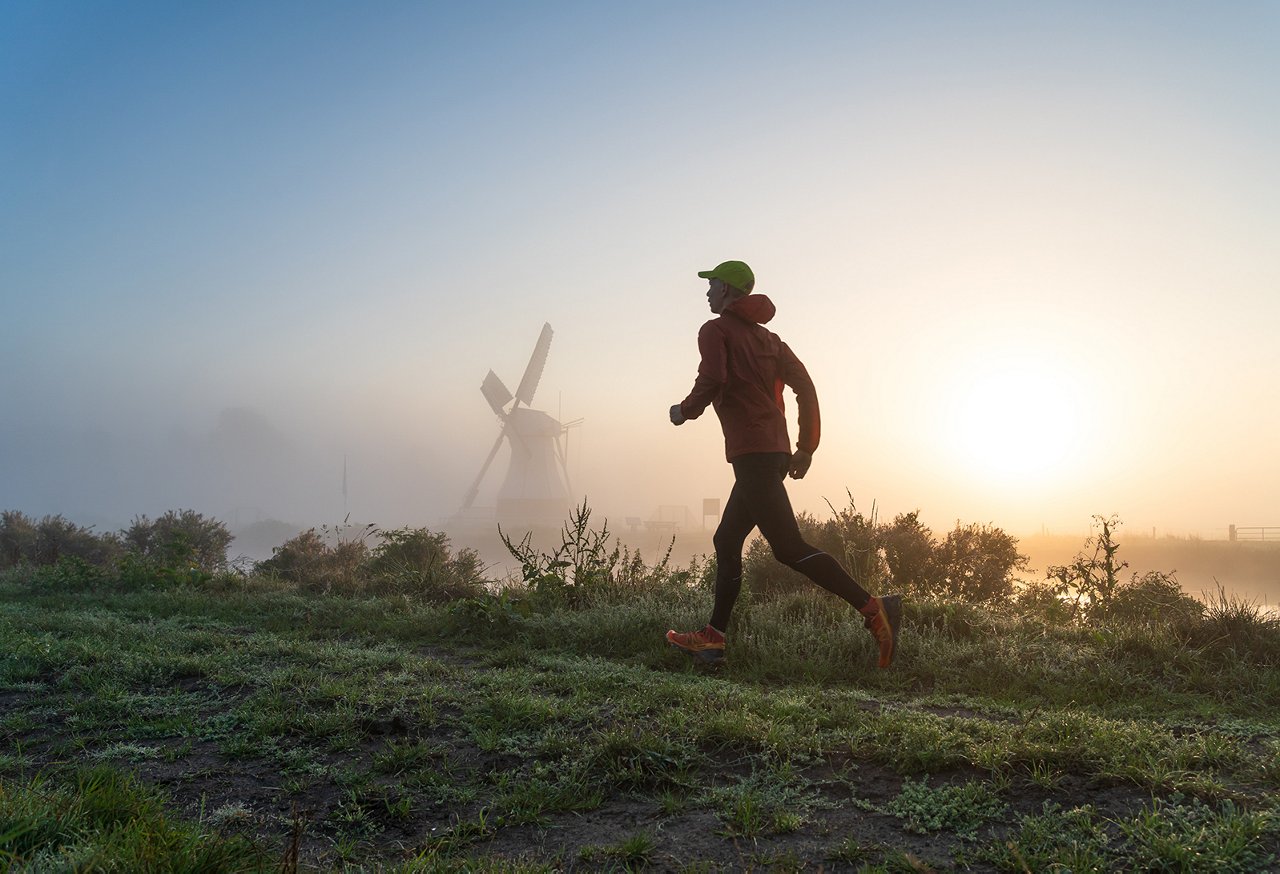 Man running in the foggy, Dutch countryside near a windmill during a tranquil sunrise. With motion blur.