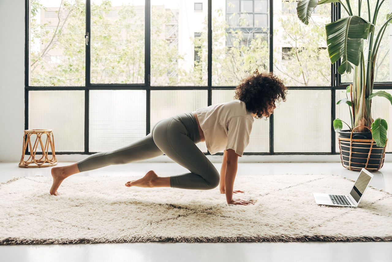 Young latina woman exercising at home using laptop to follow online fitness video tutorial. Copy space. Sport concept.