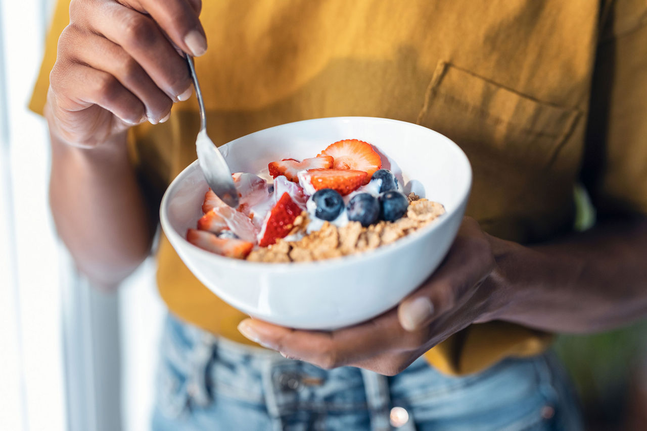 Vrouw die een kom yoghurt met muesli en fruit vasthoudt