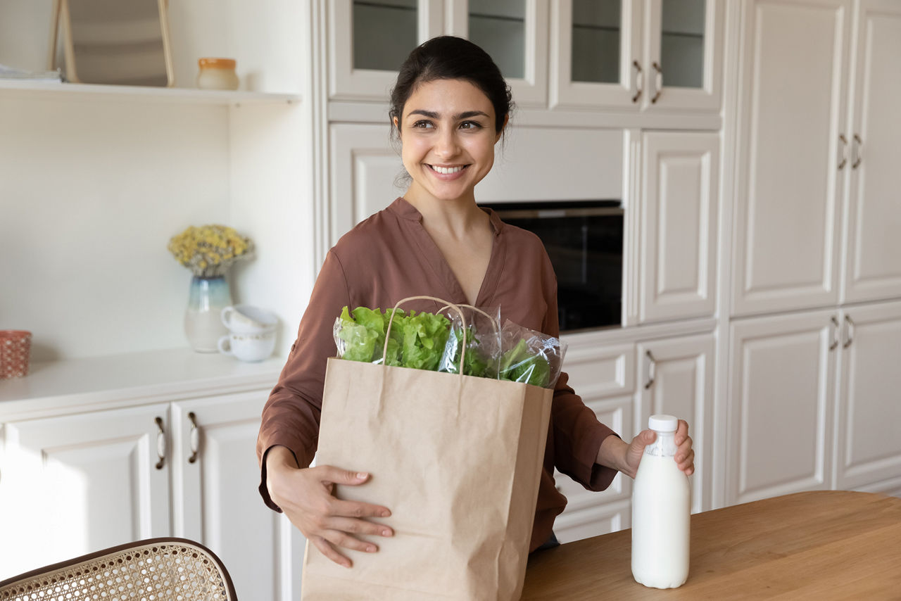 Happy millennial Indian woman shopping for healthy vegetarian organic or bio products. Smiling young ethnic female unbox package bag buy farmer goods at supermarket. Online delivery, diet concept.