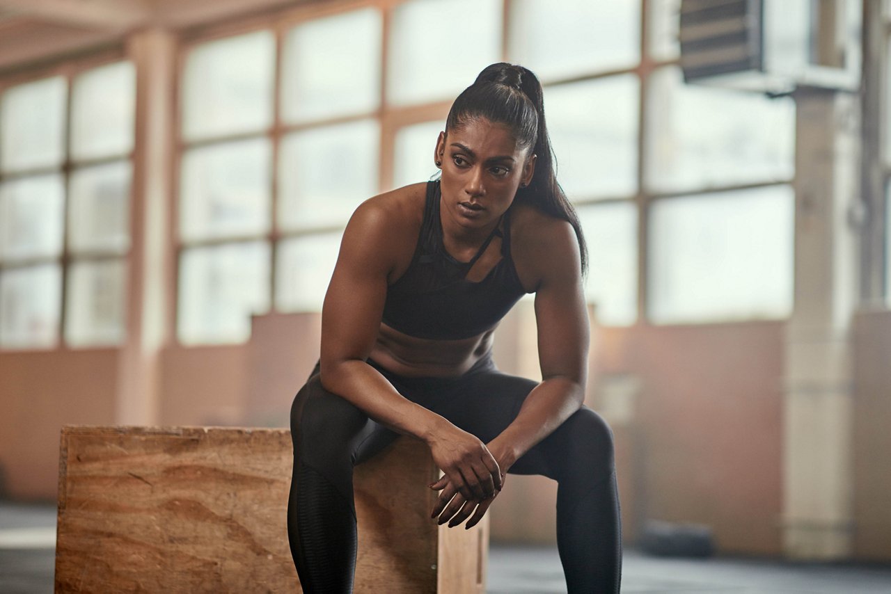 जिम में बॉक्स पर बैठी एक एथनिक महिला खिलाड़ी