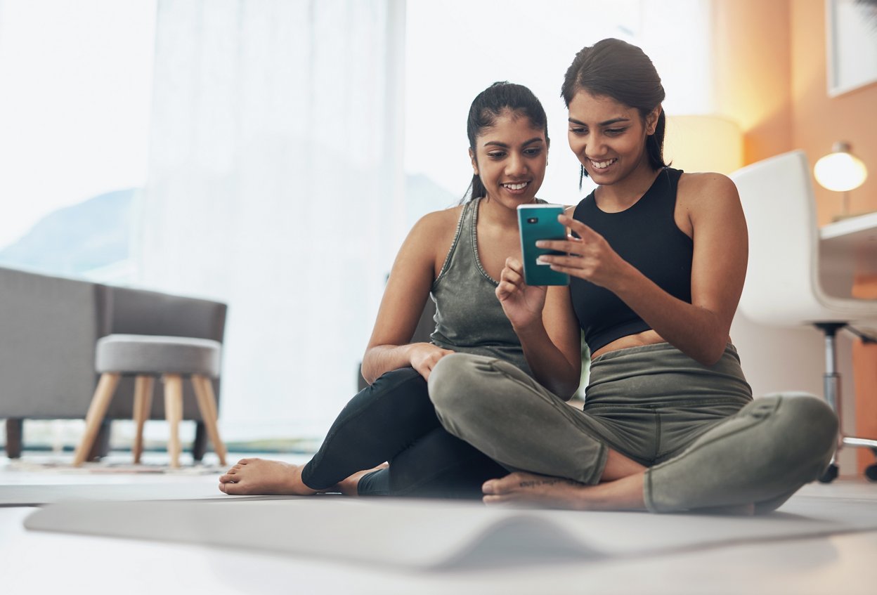 Exercise, phone and women together at home with internet connection and social media. Indian sisters or female friends in lounge with smartphone for online class, chat or fitness workout with partner.
