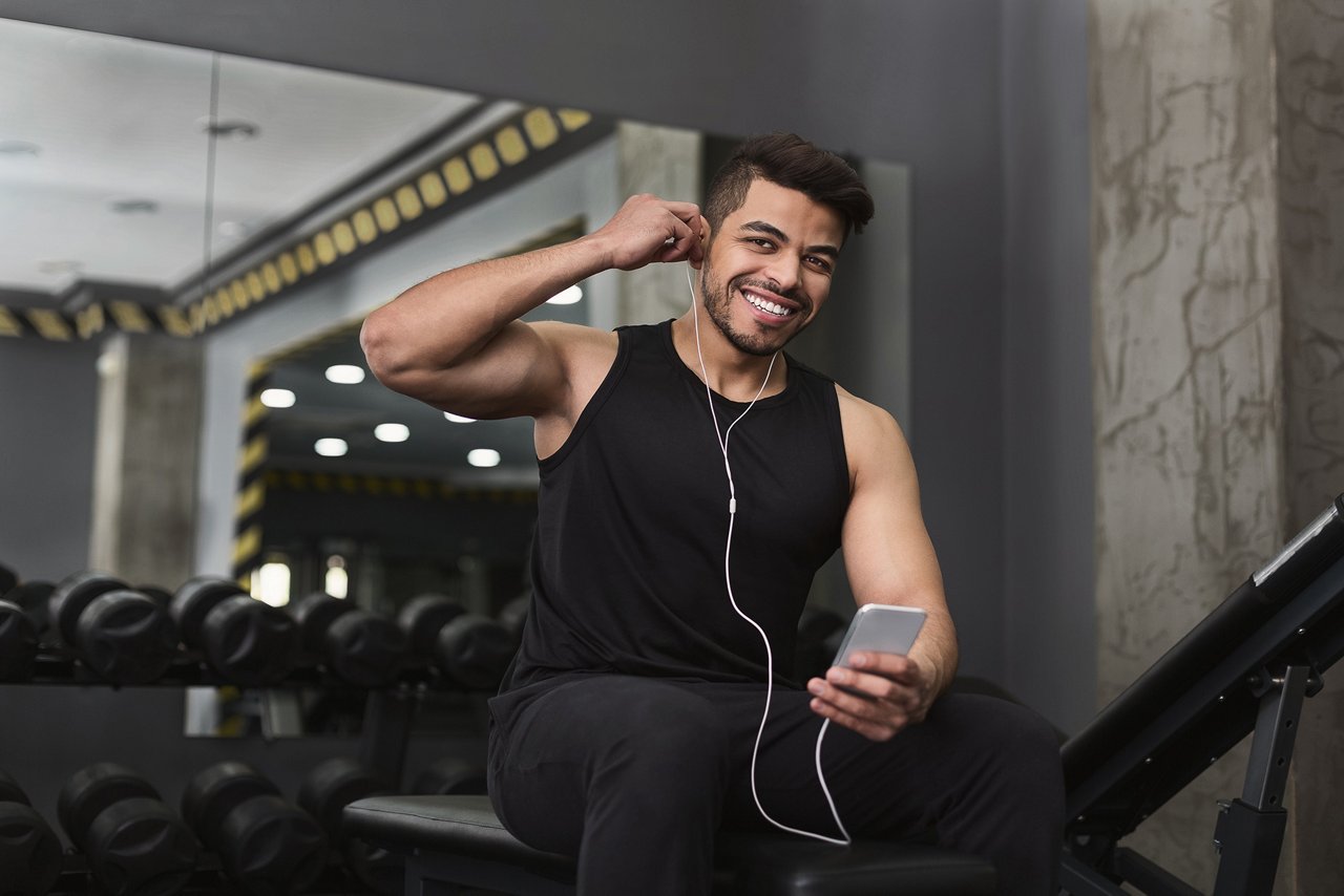 Music for sport. Happy fitness man listening music on smartphone in earphones at gym