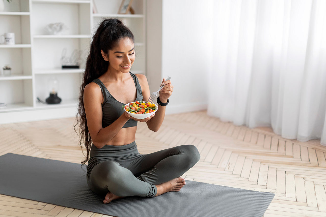 Woman Sitting With Crossed Legs On Yoga Mat Eating Lunch