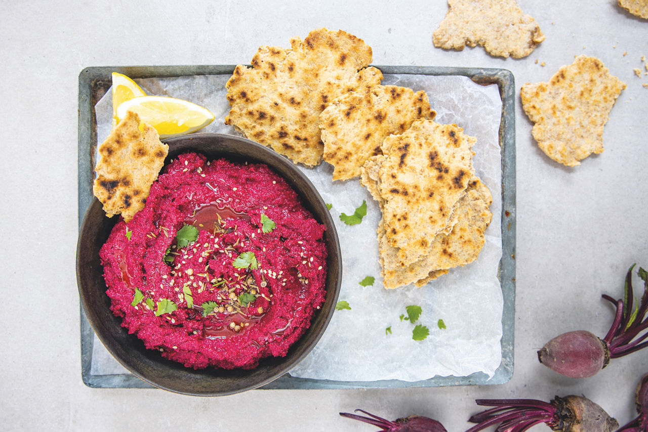 Houmous de betterave servi avec des crackers et des tranches de citron.