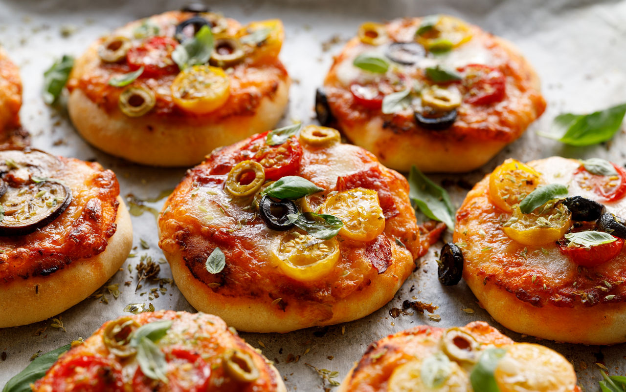 Piccole pizzette con l'aggiunta di pomodorini, olive, mozzarella e basilico fresco su uno sfondo rustico di legno