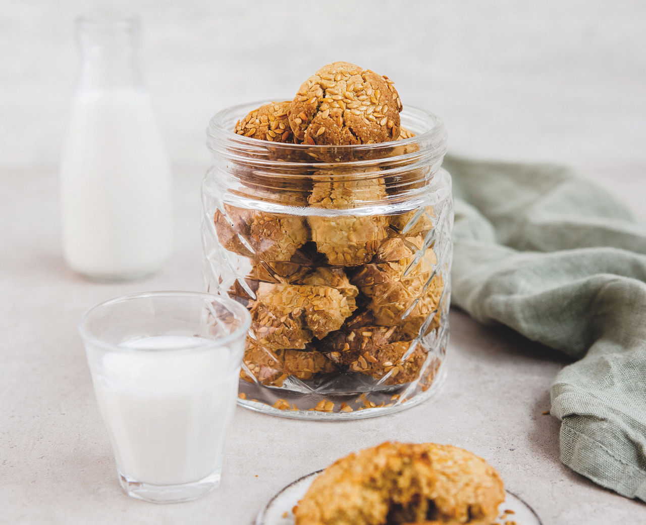 Um frasco de bolachas de amêndoa com sésamo por cima e um copo de leite