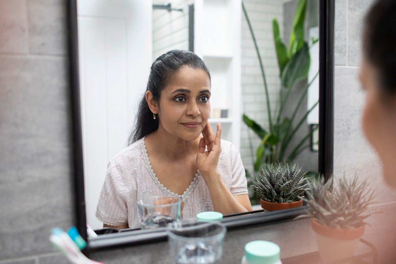 UK, London, Woman touching face reflected in bathroom mirror